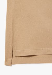 Ruskea kangas, jossa on teksturoitu kudonta, taitetut helmat ja sivuhalkiot, näyttäen ompeleet reunoilla.