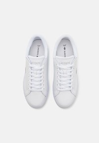 Sneakers bianchi con allacciatura, realizzati in materiale sintetico liscio, colletto imbottito, punta arrotondata e un piccolo logo verde sul lato.