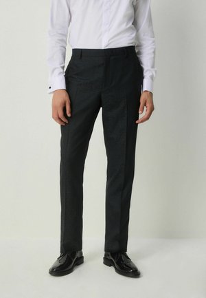 Black textured trousers with a slim fit, featuring a flat front and side pockets, paired with shiny black dress shoes.