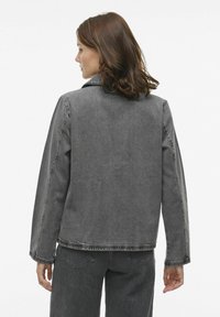 Sivá deninová bunda s dlhými rukávmi, golierom a viditeľným prešívaním; v kombinácii so zodpovedajúcimi sivými nohavicami; hladká textúra.