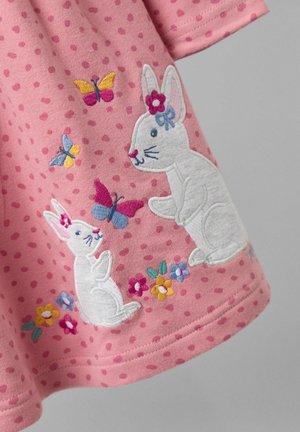 Rosa Stoff mit Punkten zeigt weiße gestickte Kaninchen, Blumen und bunte Schmetterlinge, die detaillierte Stiche und ein verspieltes Design präsentieren.