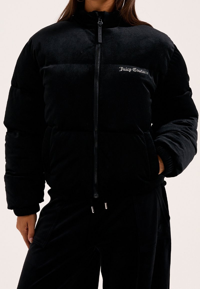 Giacca a vento nera in tessuto plush, con colletto alto, chiusura zip e polsini elastici. Logo ricamato sul petto.