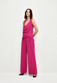 Haut sans manches fuchsia avec décolleté en V et détail de bouton, associé à un pantalon à jambes larges de la même couleur. Tissu lisse, design minimaliste.
