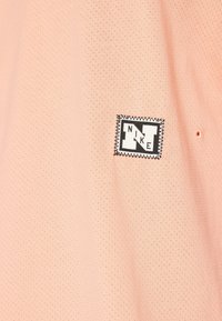 Light pink mesh polo shirt featuring a stitched black and white Nike logo patch with geometric design elements.