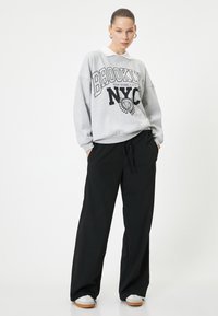 Sudadera gris con estampado "BROOKLYN NYC", cuello blanco, combinada con pantalones negros holgados y zapatillas grises con suela de goma.