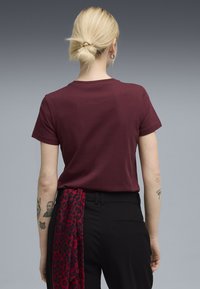 Mørkerød t-shirt med korte ærmer, rund hals og glat tekstur, iført med sorte bukser og et rødt leopardprint tørklæde bundet om taljen.