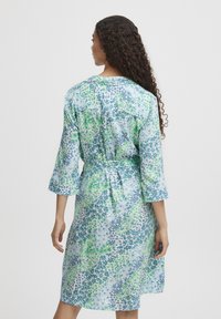 Rochie florală cu mâneci trei sferturi, având un model albastru și verde, dintr-un material moale, și talie strânsă. Vedere din spate arată detalii cu nasturi.