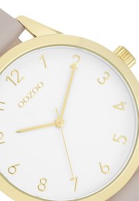 Rose gold watch with a gold-tone stainless steel case, white dial, and beige silicone strap. Features clear hour markers and hands.