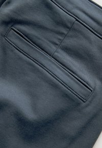 Dunkelgrauer Stoff mit glatter Textur, einem einzigen Gesäßtasche und dezenten Nähten. Keine sichtbaren Muster oder Beschläge.