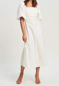 Bíl dress s střední délkou, čtveratým výstřihem, skládacím korzetem a nabíranými rukávy. Látka se zdá být hladká, s minimalistickými designovými detaily.