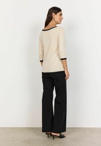 Beige, fitted top with 3/4 sleeves and black trim at the neckline and cuffs, paired with high-waisted black wide-leg pants and black heels.
