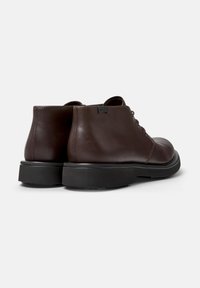 Zapatos de cuero marrón con un acabado suave, punta redondeada y suela de goma negra; cuentan con cinco ojetes para los cordones y un pequeño acento de logo.