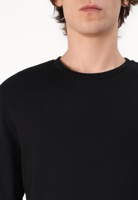 Melna Crew Neck džemperis, izgatavots no gludas auduma. Ar garām piedurknēm un brīvu piegriezumu, ar ribinātu apkakli, lai pievienotu papildu detaļas.