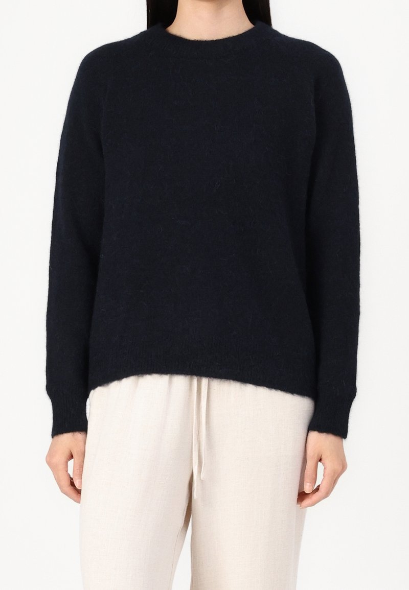 Pull en maille bleu marine à manches longues, col rond et coupe décontractée. Texture douce, légèrement plus long à l'arrière avec des poignets côtelés.