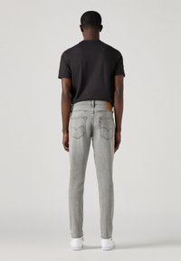 Jeans grii ajustați cu o ușoară decolorare, având buzunare din spate clasice și un etichetă din piele maro. Asortați cu un tricou negru simplu și pantofi albi.