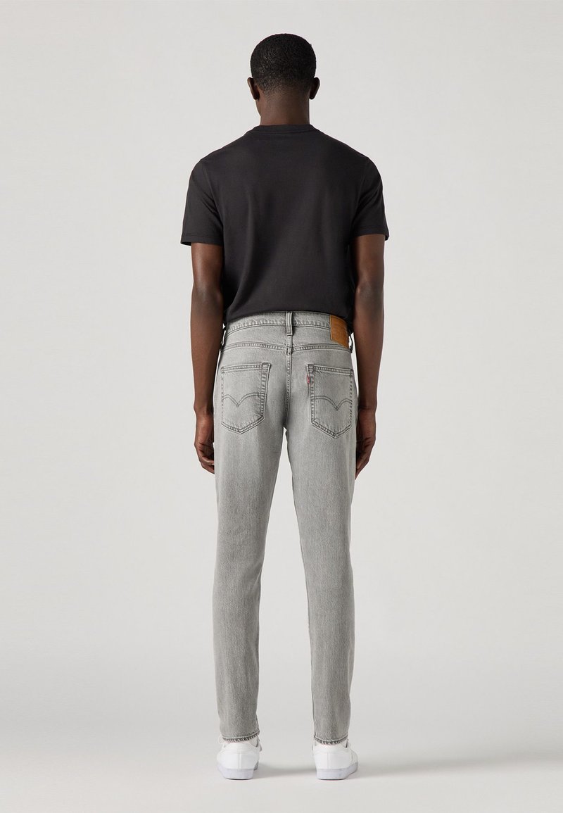 Aansluitende grijze jeans met een lichte vervaging, voorzien van klassieke achterzakken en een bruine leren label. Gemaakt met een eenvoudig zwart T-shirt en witte schoenen.