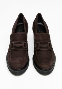 Mocassins en suède marron avec un embout carré, dotés d'une accentuation de boucle décorative et d'une semelle en caoutchouc noir épaisse. Texture lisse et couture minimale.