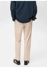 Béžové kalhoty s rovný střihem, vyrobené z lehké tkaniny. Nošeny s tmavě modrou košilí a černými sandály s plochou podrážkou a pásky kolem kotníků.