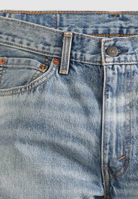 Ljusblå denimjeans med en urblekt finish. Har mässingsbeslag, orange sömmar och en klassisk design med fem fickor.