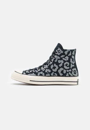 Zwarte hoge sneaker met grijze luipaardprint, witte rubberen zool en zwarte veters, zijkant zichtbaar op een witte achtergrond.