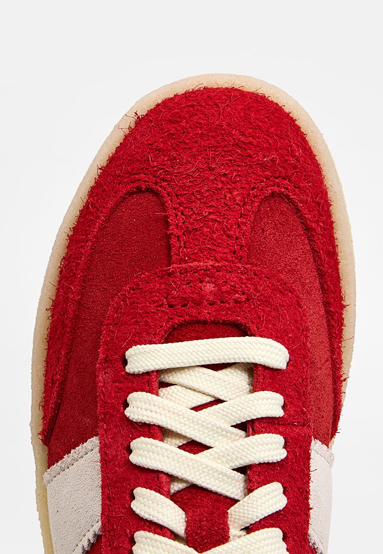 Baskets rouges avec un mélange de daim texturé et de tissu lisse, lacets crème et semelle en caoutchouc beige avec une bande latérale blanche.