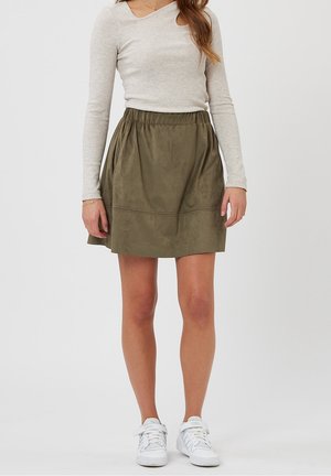 Jupe olive, longueur genou, avec une texture lisse, taille élastique et poches latérales, associée à un haut à manches longues gris clair et des baskets blanches.