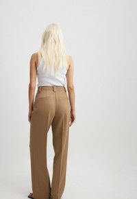 Pantalons taille haute beiges avec une coupe structurée, dotés de poches arrière et d'une texture lisse, associés à un débardeur blanc.