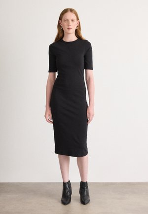 Black fitted midi dress with short sleeves, smooth texture, crew neckline, and knee-length hem. Worn with black ankle boots.