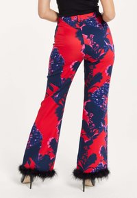 Flared pants in a vibrant red fabric featuring large floral patterns in navy and pink. Trimmed with black faux fur at the hem.