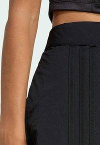 Czarne spodenki sportowe z teksturowanej tkaniny, szerokim pasem w talii i trzema pionowymi paskami elastycznymi po boku.