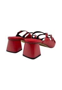 Zapatos rojos de punta descubierta con un acabado suave, que presentan un tacón grueso y tiras entrecruzadas. La planta interior está acolchada con una ligera textura.