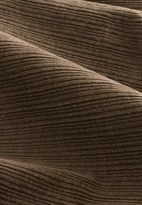 Brunt kordfløjl, der har en ribbet overflade med flere lodrette ribber. Materialet ser blødt og varmt ud, med subtile farvevariationer.
