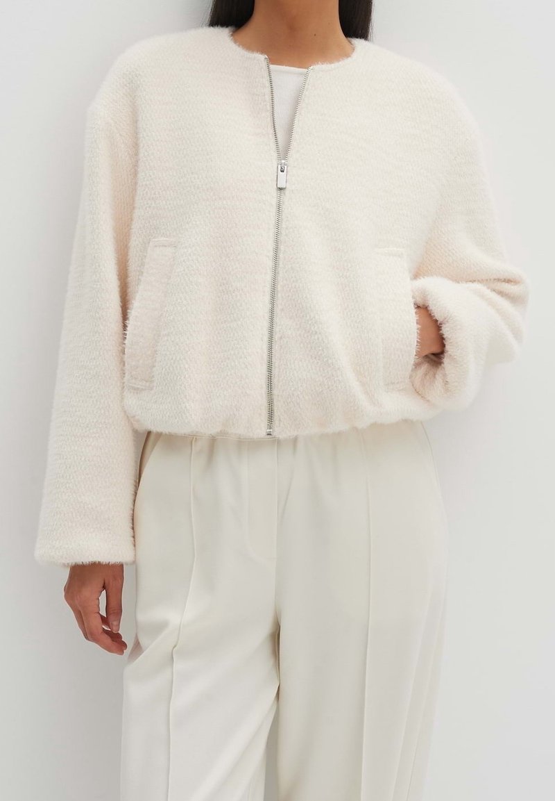 Ljust rosa, texturerad zip-up jacka med rund hals, två sidofickor och lös passform, i kombination med krämfärgade byxor.