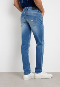 Dopasowane niebieskie dżinsy z lekkim przecieraniem, pięcioma kieszeniami i logotypem na tylnej talii. Zestawione z białymi trampkami.