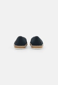 Navy canvas slip-on shoes with beige braided jute sole, featuring a round back and embossed logo on the heel.