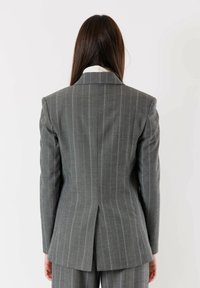 Blazer grigio a righe con vestibilità sagomata, rever a scialle e spacco posteriore. Presenta una texture del tessuto liscia e una silhouette sartoriale.