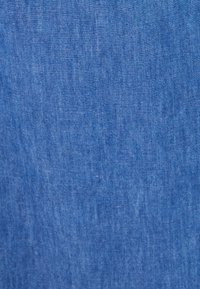 Tejido de denim en un tono azul medio, con una textura sutil y ligeras variaciones. Sin patrones visibles ni detalles notables.