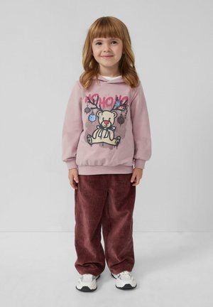 Lichtroze sweatshirt met berenafbeelding en tekst, gecombineerd met brede bordeauxrode corduroypantalon. Kind draagt witte sneakers. Strakke pasvorm.