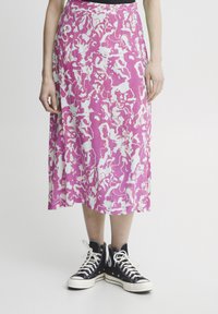 Falda de patrón rosa y blanco hecha de una tela ligera, hasta la rodilla con un diseño fluido, combinada con zapatillas negras de caña alta.
