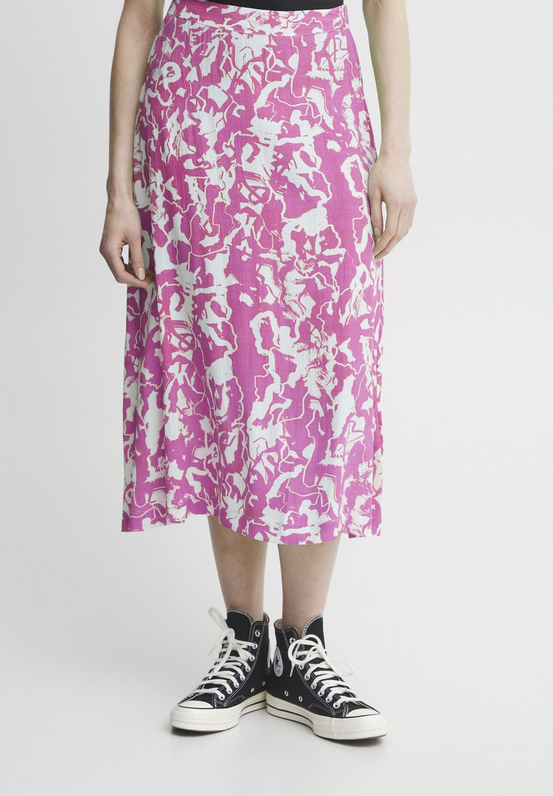 Falda de patrón rosa y blanco hecha de una tela ligera, hasta la rodilla con un diseño fluido, combinada con zapatillas negras de caña alta.