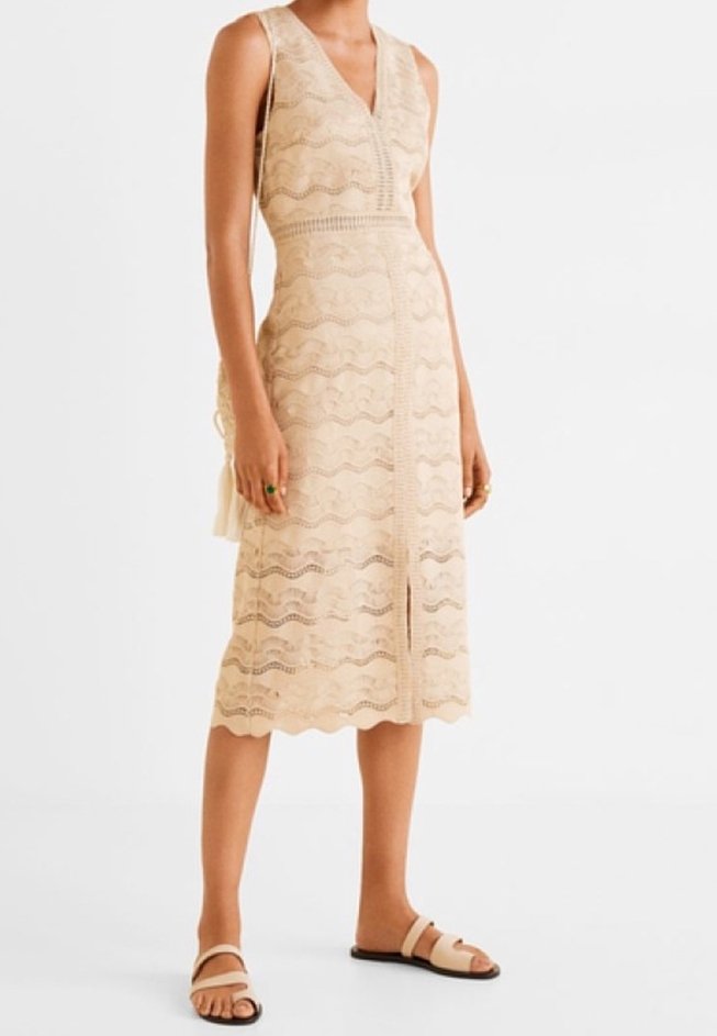 Robe midi en dentelle beige avec un motif ondulé, décolleté en V et une fente devant. Associée à des sandales plates.