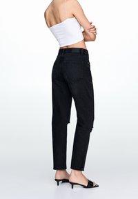 Vaqueros negros de talle alto con corte relajado, que presentan dobladillos deshilachados, cinco bolsillos y una textura de denim resistente, combinados con mule negros de tacón.