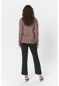 Roze gebreide sweater met lange mouwen, geribbelde manchetten en zoom, gecombineerd met zwarte, licht flare broek en sandalen met hoge hakken en bandjes.