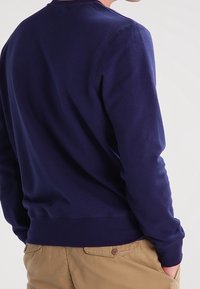 Sweatshirt bleu marine avec col rond, poignets et ourlet côtelés. Tissu doux, coupe ajustée, design uni sans motifs ni accents.