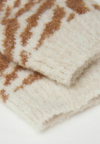 Strikket uldstof i creme med brune abstrakte bølgemønstre, der har en blød, fuzzy tekstur og foldede kanter.