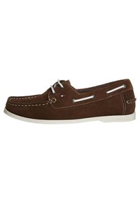 Zapato náutico de ante marrón con costuras y cordones blancos, con ojales laterales y suela de goma blanca. Detalle del logo cerca del talón.