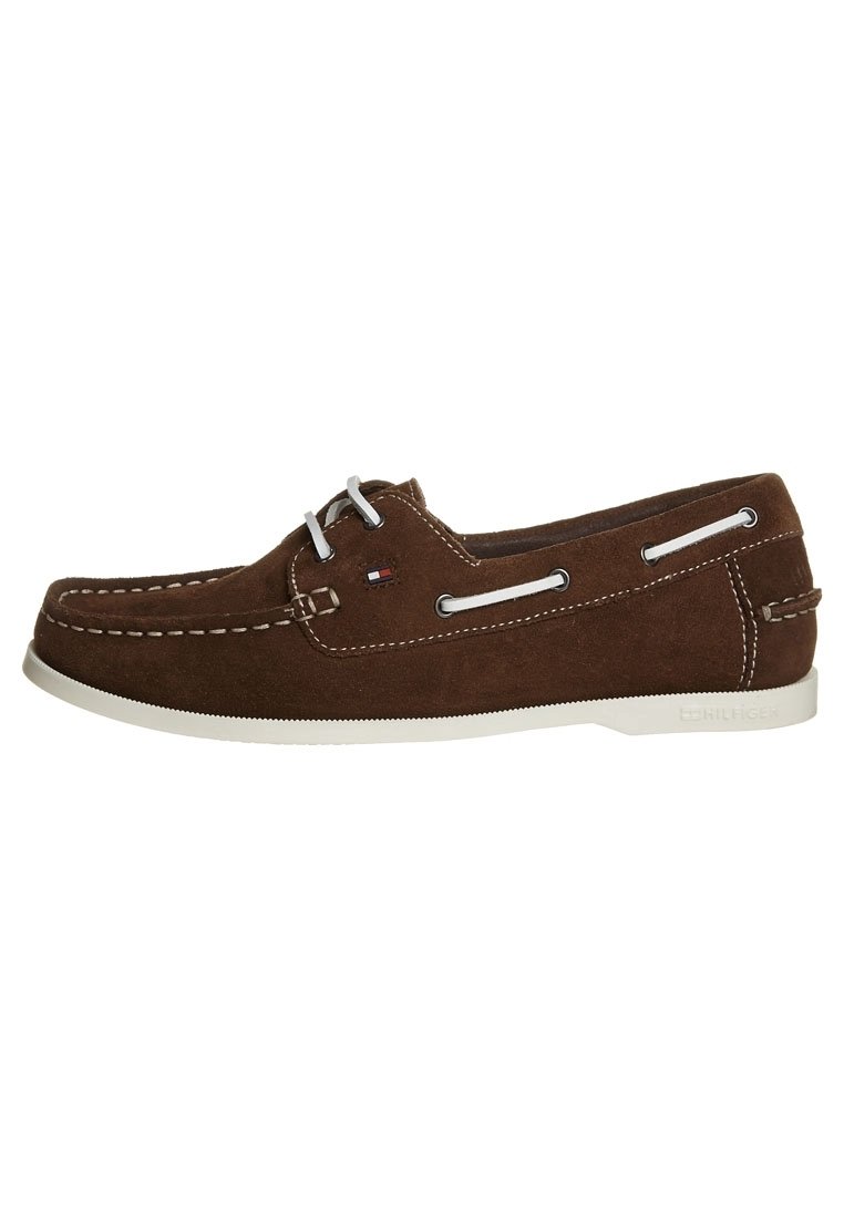 Zapato náutico de ante marrón con costuras y cordones blancos, con ojales laterales y suela de goma blanca. Detalle del logo cerca del talón.