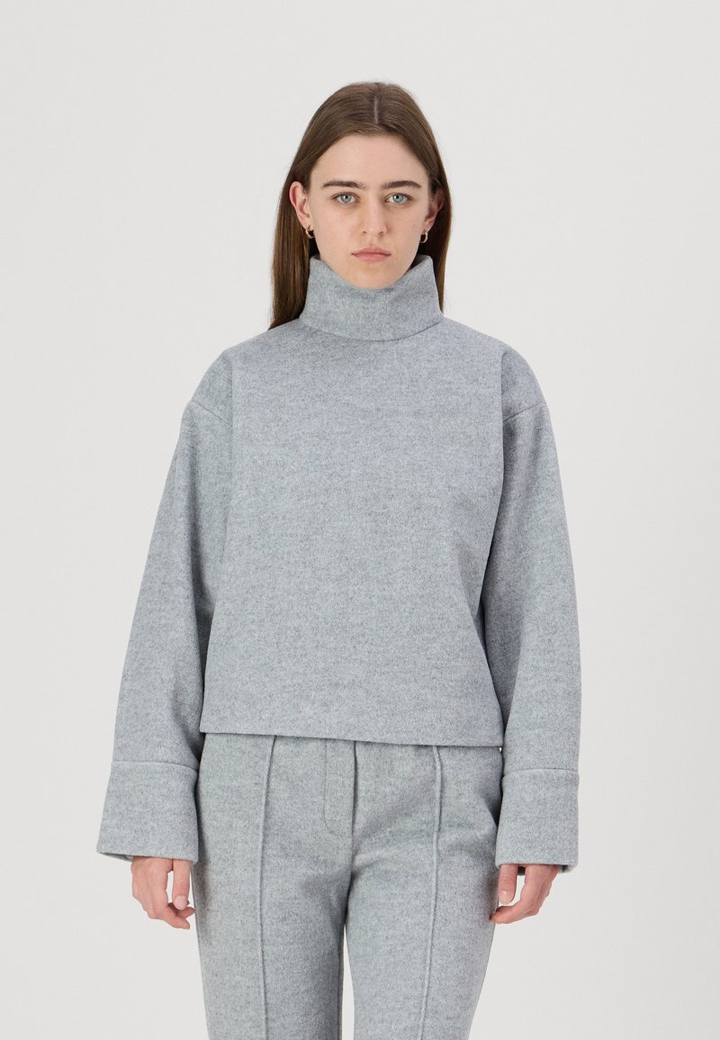 Grå, teksturert turtleneck genser og matchende høy midje bukser. Avslappet passform med brede ermer og synlige sømdetaljer.