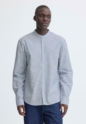 Hellgraues Hemd mit durchgehender Knopfleiste, Stehkragen, langen Ärmeln und feiner Struktur. Kombiniert mit dunklen Denim-Hosen.