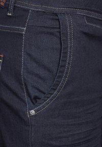 Jeans de mezclilla azul oscuro con costuras amarillas en contraste, que cuentan con bolsillos frontales en ángulo y detalle de botón plateado en el lado.